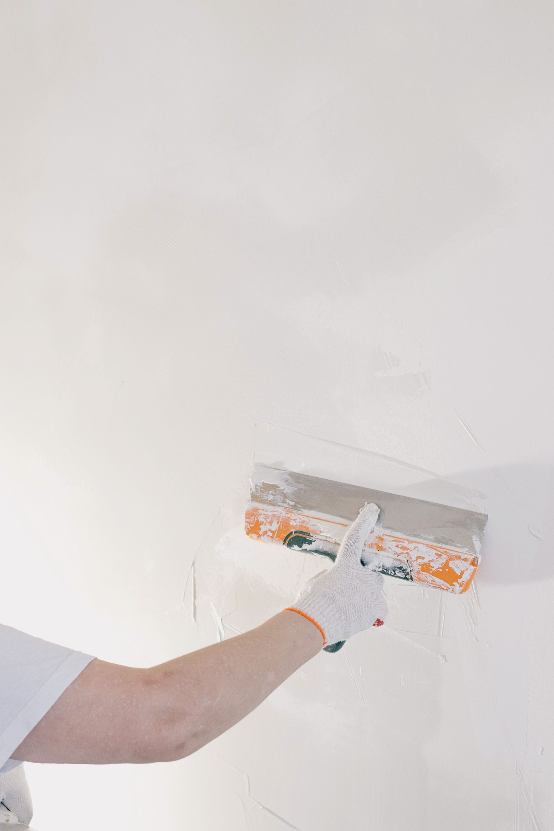 Crop anonymous male in gloves holding spatula and plastering walls in room at home